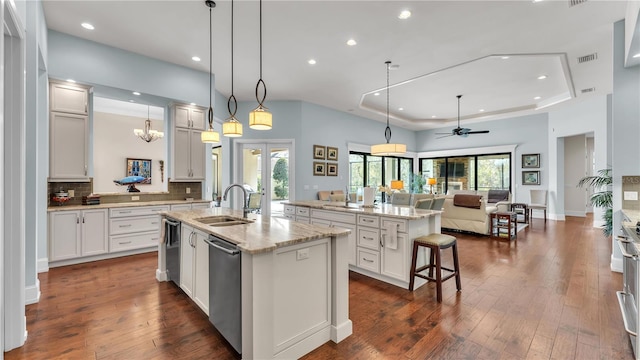 kitchen featuring sink, a tray ceiling, an island with sink, pendant lighting, and white cabinets