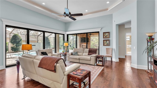 living room with a tray ceiling, dark hardwood / wood-style floors, ceiling fan, and a towering ceiling