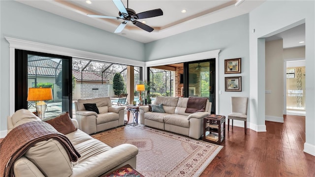 living room with a towering ceiling, dark hardwood / wood-style floors, ceiling fan, and a tray ceiling