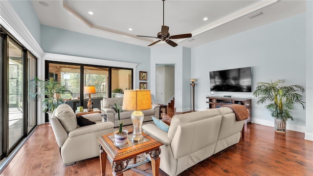 living room featuring a tray ceiling, dark wood-type flooring, ceiling fan, and a towering ceiling