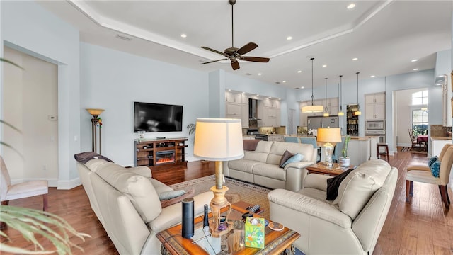 living room with dark hardwood / wood-style flooring, a raised ceiling, and ceiling fan