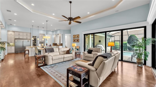 living room featuring dark hardwood / wood-style floors, ceiling fan, and a tray ceiling