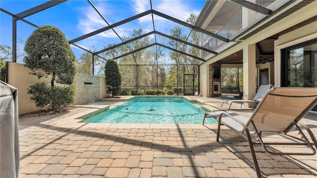 view of pool with ceiling fan, a fireplace, glass enclosure, and a patio