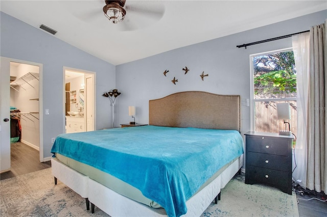 bedroom with connected bathroom, wood-type flooring, a spacious closet, vaulted ceiling, and ceiling fan