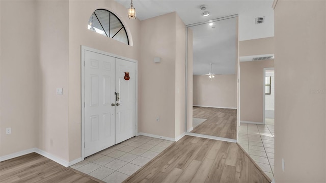 foyer featuring a towering ceiling, ceiling fan, and light wood-type flooring