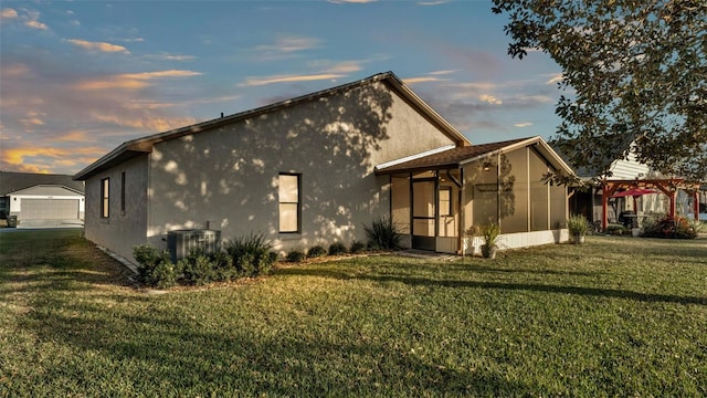 property exterior at dusk featuring a yard, a pergola, a sunroom, and central air condition unit