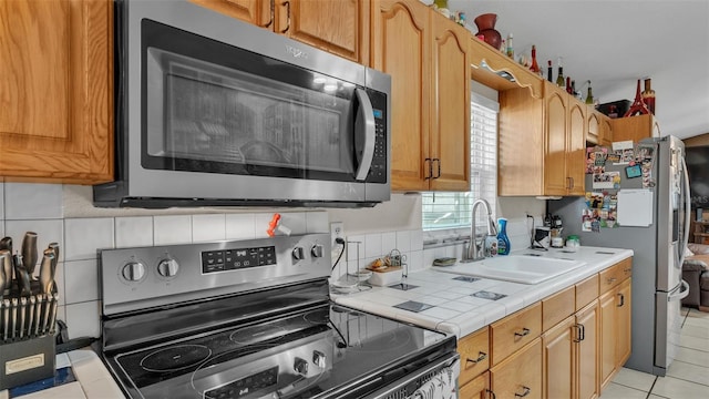 kitchen featuring light tile patterned floors, stainless steel appliances, a sink, tile counters, and tasteful backsplash