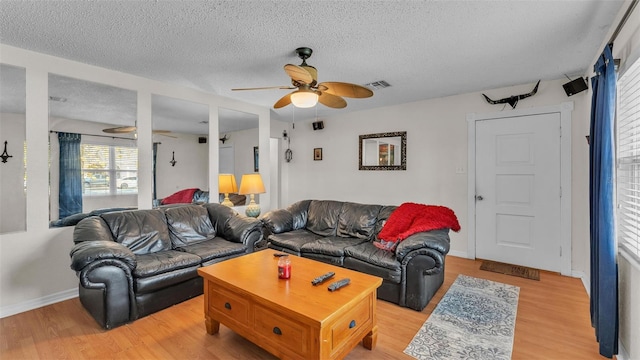 living area with a ceiling fan, visible vents, light wood-style flooring, and a textured ceiling