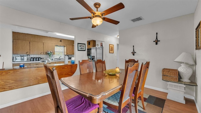 dining area with ceiling fan, light wood finished floors, visible vents, and baseboards