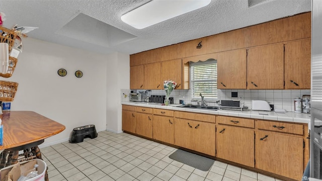 kitchen with light tile patterned floors, tile counters, a sink, a textured ceiling, and backsplash