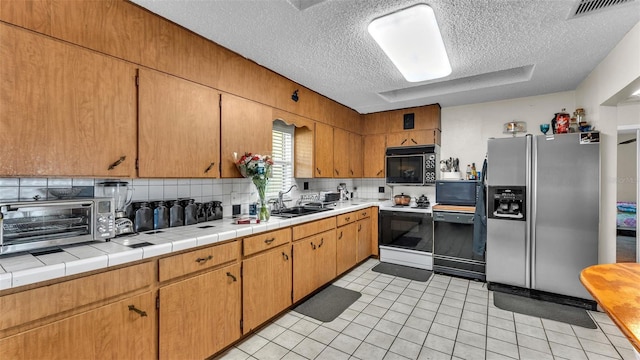 kitchen featuring electric range, visible vents, black microwave, stainless steel refrigerator with ice dispenser, and a sink