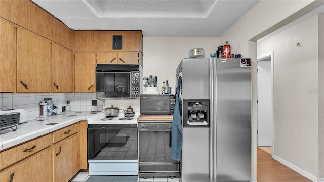 kitchen featuring electric range, tasteful backsplash, tile countertops, black microwave, and stainless steel refrigerator with ice dispenser