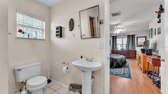 half bathroom with connected bathroom, toilet, wood finished floors, visible vents, and baseboards