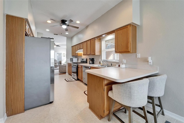 kitchen featuring appliances with stainless steel finishes, a breakfast bar, sink, ceiling fan, and kitchen peninsula