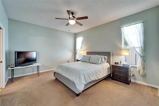 bedroom with ceiling fan, light colored carpet, and a textured ceiling