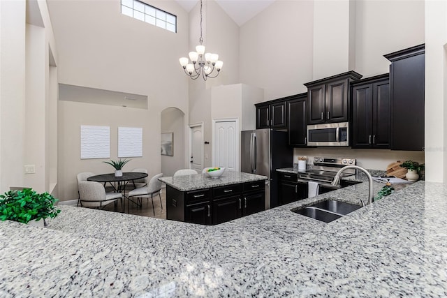 kitchen with sink, stainless steel appliances, light stone counters, decorative light fixtures, and a chandelier