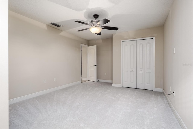 unfurnished bedroom featuring ceiling fan, a closet, light carpet, and a textured ceiling