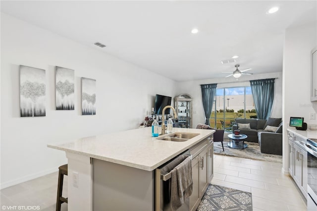 kitchen with sink, a breakfast bar, dishwasher, ceiling fan, and a kitchen island with sink