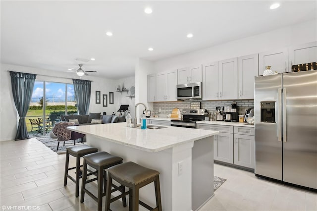 kitchen with sink, a kitchen bar, stainless steel appliances, light stone countertops, and a center island with sink