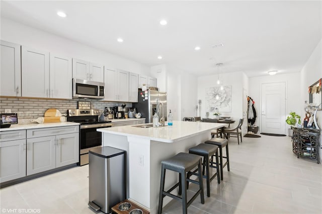 kitchen featuring an island with sink, appliances with stainless steel finishes, decorative backsplash, and decorative light fixtures