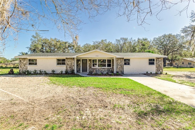 single story home featuring stone siding, driveway, and a front lawn