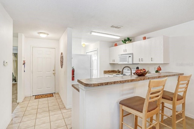 kitchen featuring white cabinetry, white appliances, a breakfast bar area, and kitchen peninsula