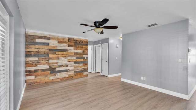 spare room with wood walls, ceiling fan, and light wood-type flooring