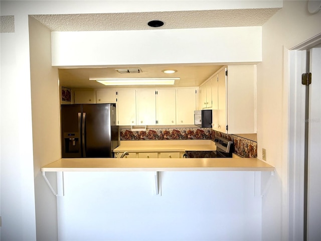 kitchen with a kitchen breakfast bar, kitchen peninsula, white cabinets, and appliances with stainless steel finishes