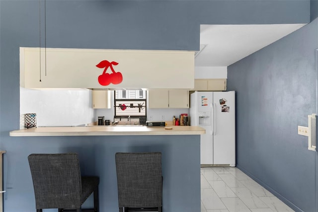 kitchen featuring cream cabinetry, white refrigerator with ice dispenser, and kitchen peninsula