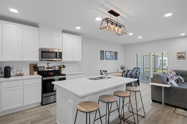 kitchen featuring sink, hanging light fixtures, stainless steel appliances, an island with sink, and white cabinets