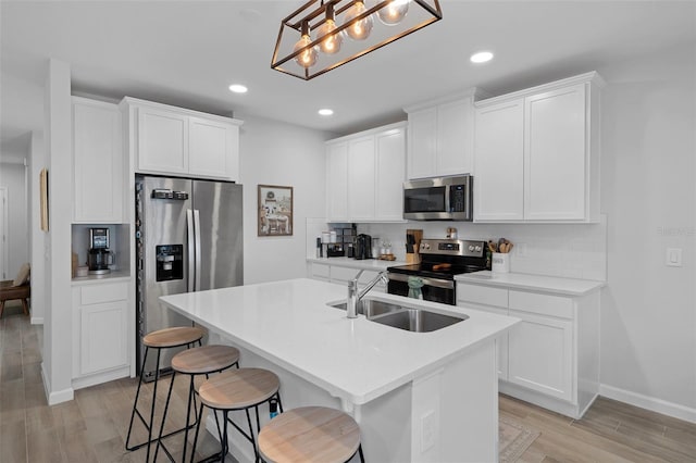 kitchen with pendant lighting, sink, white cabinetry, stainless steel appliances, and a center island with sink