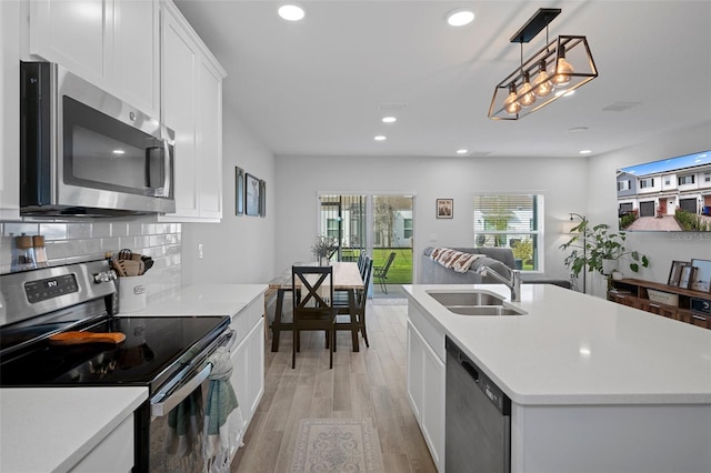 kitchen with sink, backsplash, stainless steel appliances, an island with sink, and white cabinets