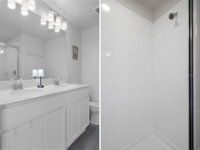 bathroom with a tile shower, vanity, and toilet