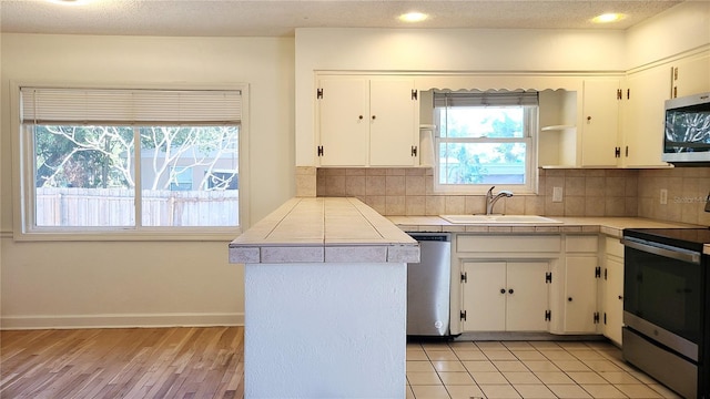 kitchen featuring sink, white cabinetry, tile countertops, appliances with stainless steel finishes, and kitchen peninsula