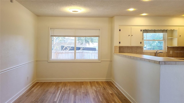 kitchen with white cabinetry, a textured ceiling, decorative backsplash, and light wood-type flooring