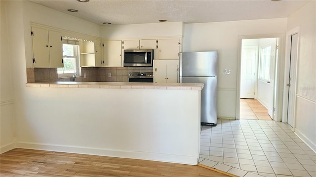 kitchen with decorative backsplash, tile counters, stainless steel appliances, and kitchen peninsula