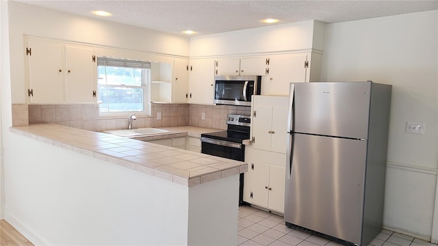 kitchen featuring white cabinetry, stainless steel appliances, tile countertops, and sink