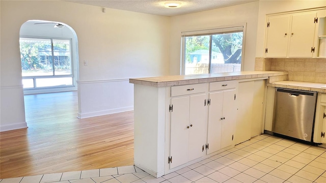 kitchen with a textured ceiling, tile counters, stainless steel dishwasher, and white cabinets