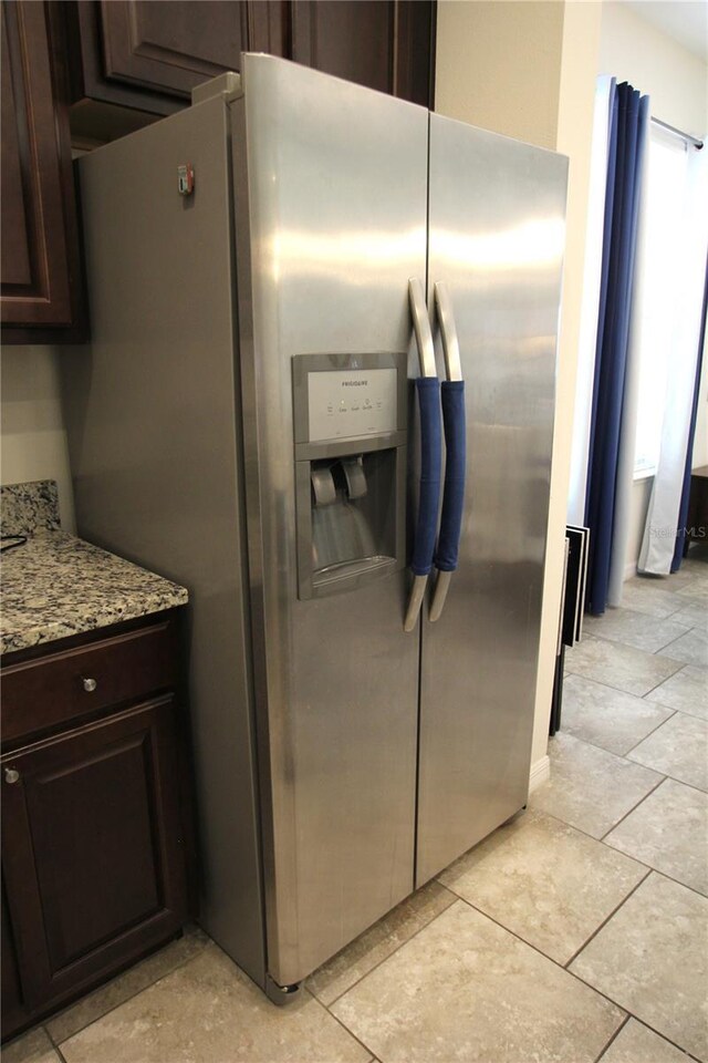 kitchen featuring light tile patterned flooring, dark brown cabinets, light stone countertops, and stainless steel refrigerator with ice dispenser