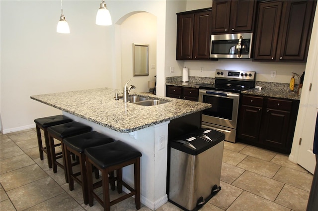 kitchen featuring sink, decorative light fixtures, stainless steel appliances, and a center island with sink