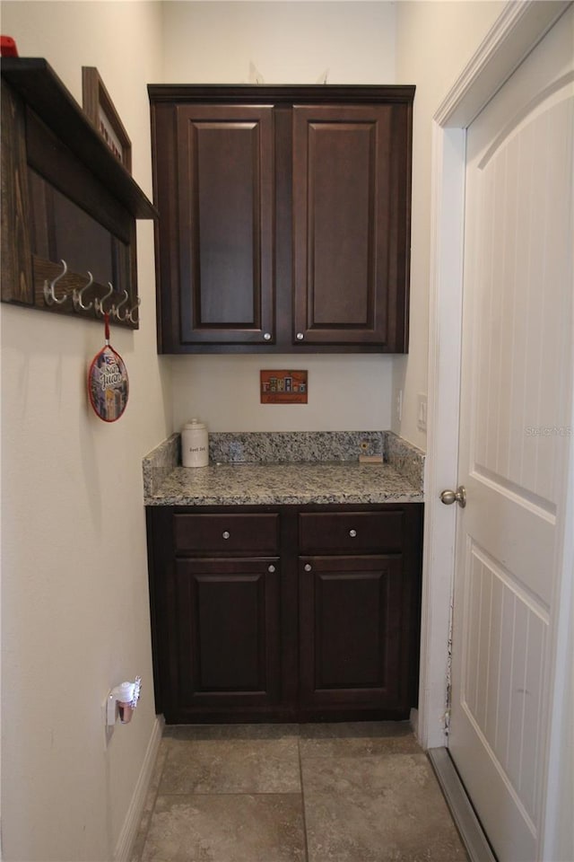 bar with light stone countertops and dark brown cabinets