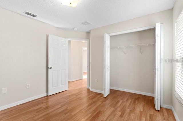 unfurnished bedroom featuring light hardwood / wood-style flooring, a closet, and a textured ceiling