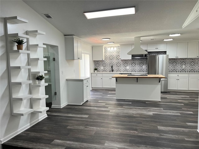 kitchen featuring island range hood, stainless steel refrigerator, white cabinetry, butcher block counters, and dark wood-type flooring