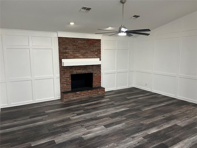 unfurnished living room with a brick fireplace, dark wood-type flooring, and ceiling fan