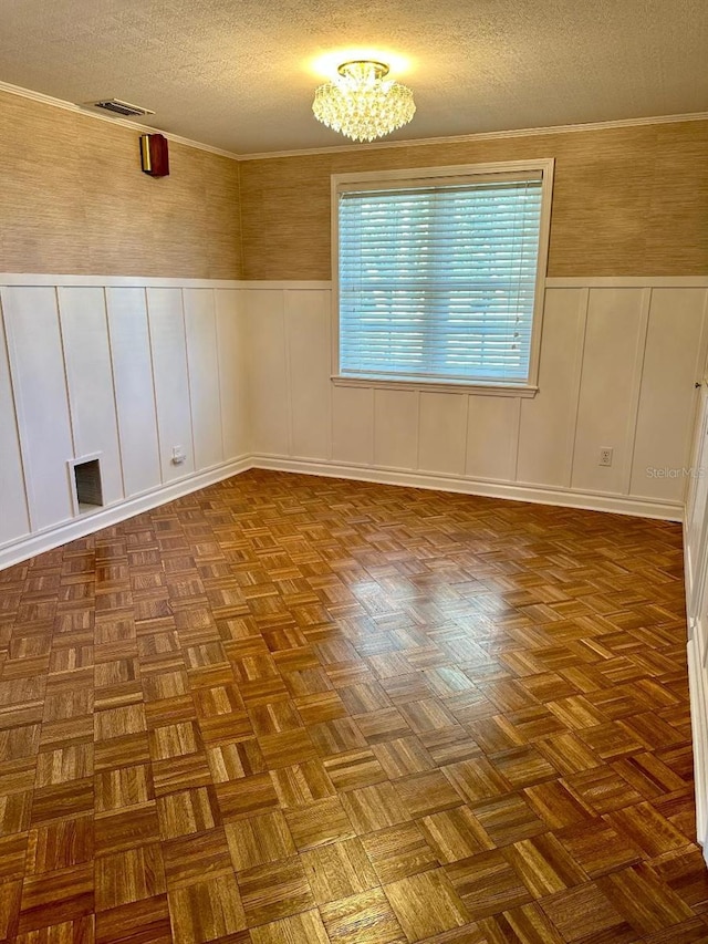 empty room featuring a textured ceiling, visible vents, and crown molding