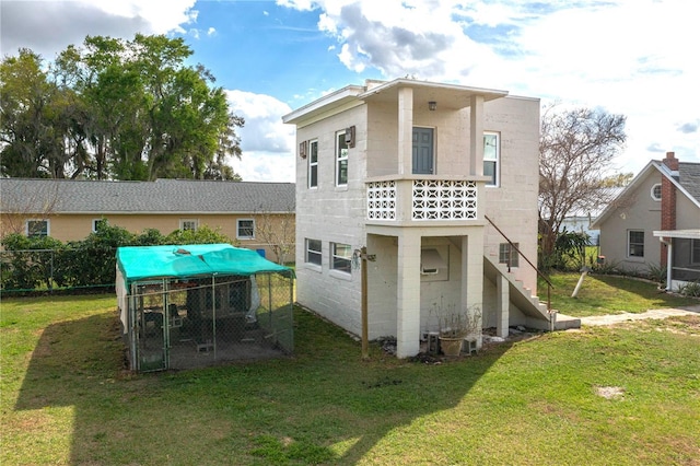 rear view of house with stairs, a yard, an outdoor structure, and concrete block siding