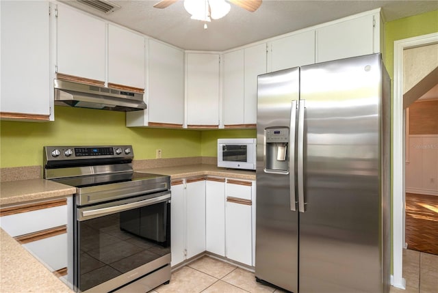 kitchen with light tile patterned flooring, under cabinet range hood, white cabinetry, light countertops, and appliances with stainless steel finishes