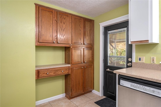 kitchen featuring dishwasher, light countertops, a textured ceiling, built in desk, and light tile patterned flooring