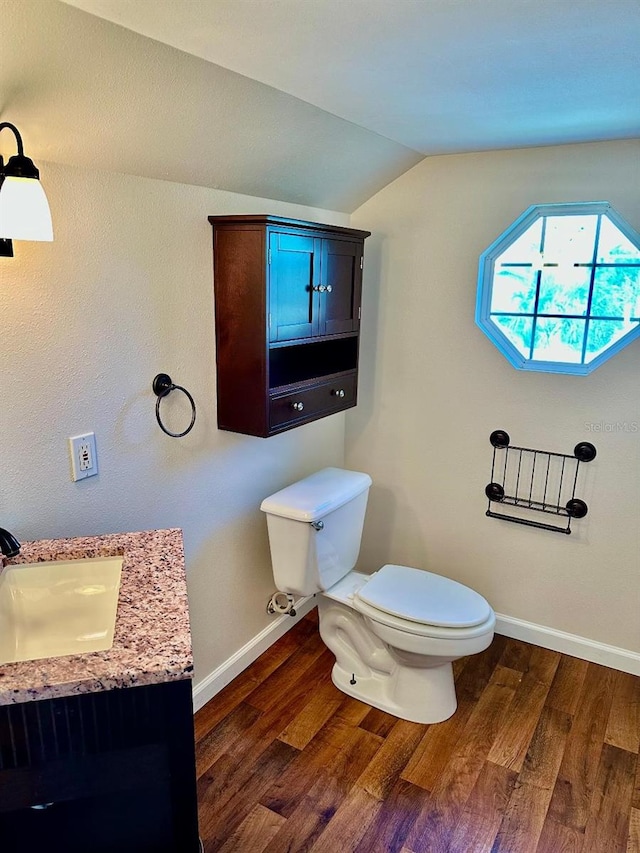 bathroom with baseboards, toilet, wood finished floors, vaulted ceiling, and vanity