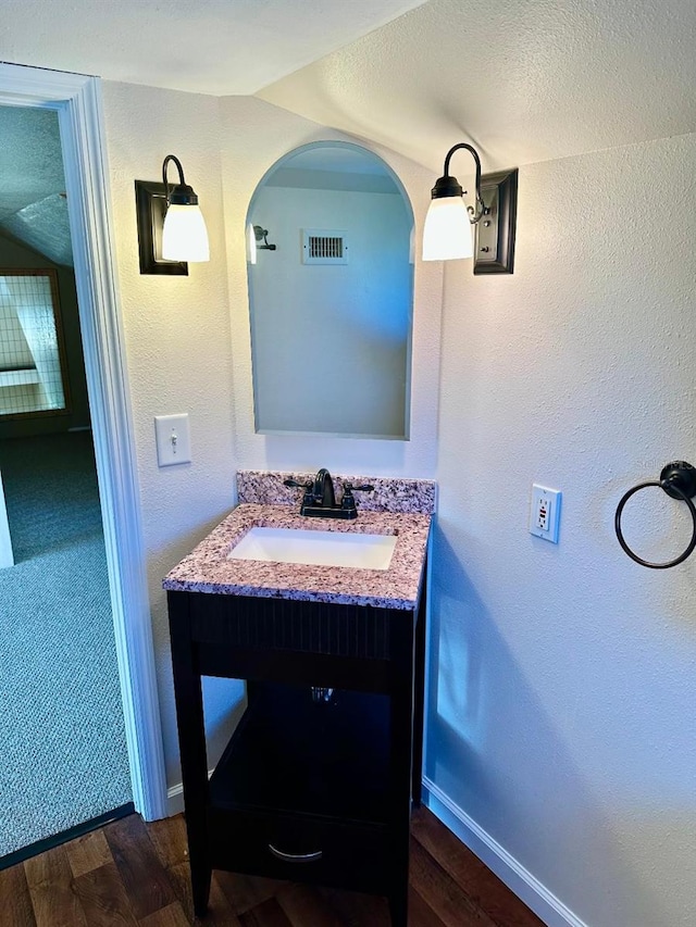 bathroom with visible vents, a textured wall, vanity, wood finished floors, and baseboards